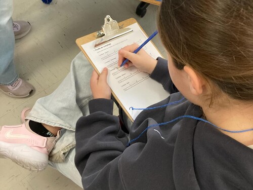 Élève prise de dos qui a une planche à documents avec une feuille sur laquelle elle consigne la compilation des votes