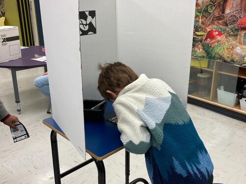 Élève qui vote au poste de scrutin devant un isoloir d'Élections Canada