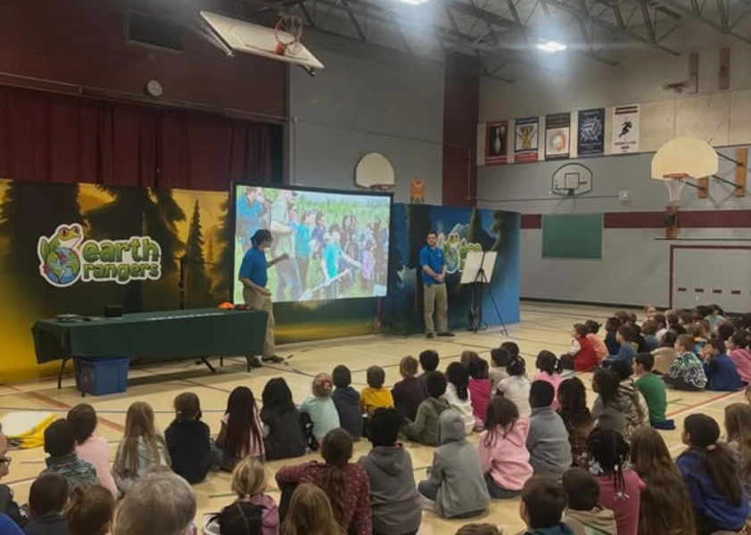 photo des élèves assis au gymnase avec 2 animateurs qui donnent une présentation devant un grand écran 
