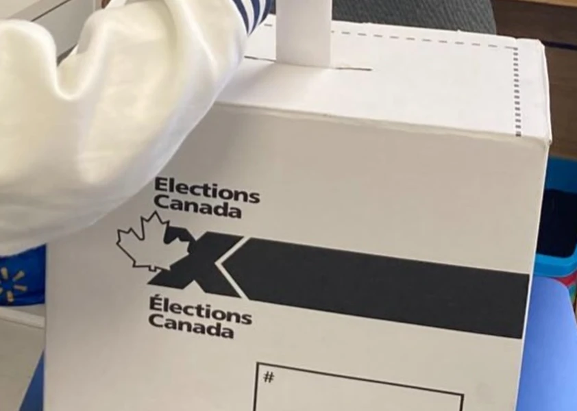 Boîte récipiente des bulletins de vote d'Élections Canada, la main d'un élève qui y met son bulletin de vote replié