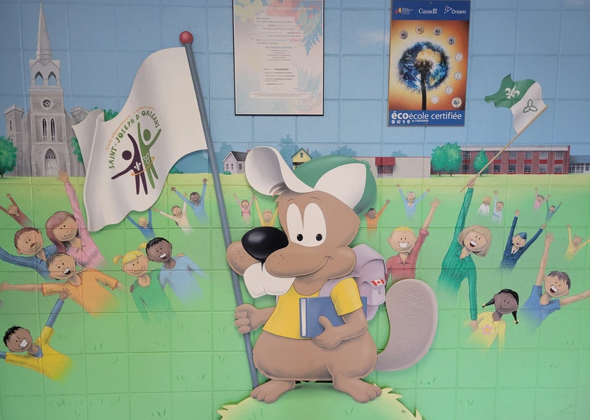 Murale colorée à l'entrée de l'école montrant la mascotte de SJO tenant un drapeau et entourée d'enfants joyeux.