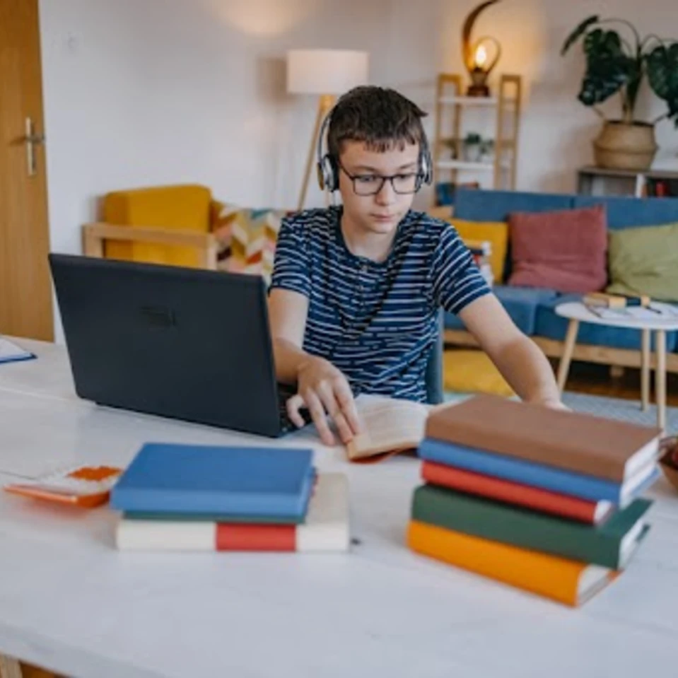 Un élève étudie à la maison devant son ordinateur portable avec des livres et des écouteurs.