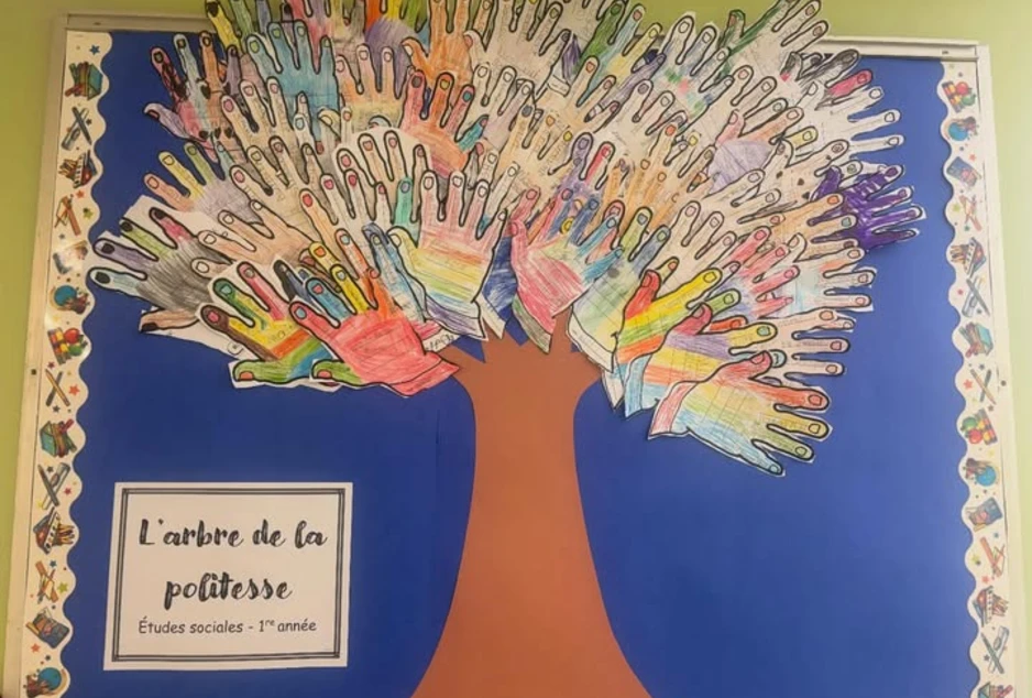 Tableau murale, grand tronc, les feuilles sont les tracés des mains des élèves, sur chaque main se retrouve des mots de politesse utilisés quotidiennement (au revoir, bonjour, merci) 