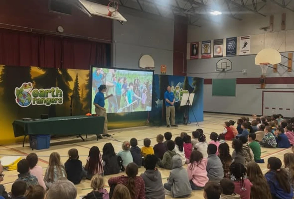 photo des élèves assis au gymnase avec 2 animateurs qui donnent une présentation devant un grand écran 